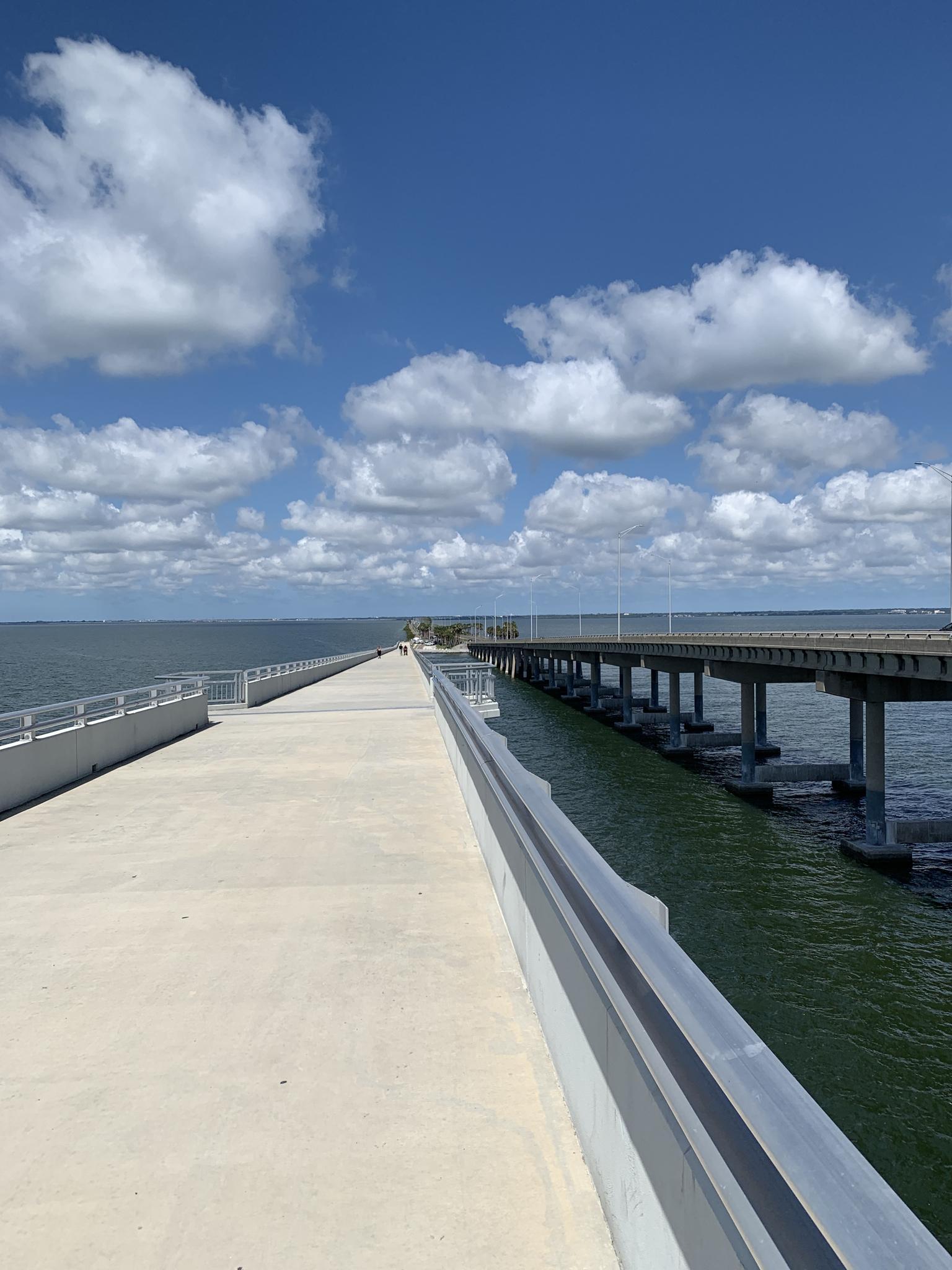 Concrete pier and highway bridge over the ocean under a partly cloudy sky.