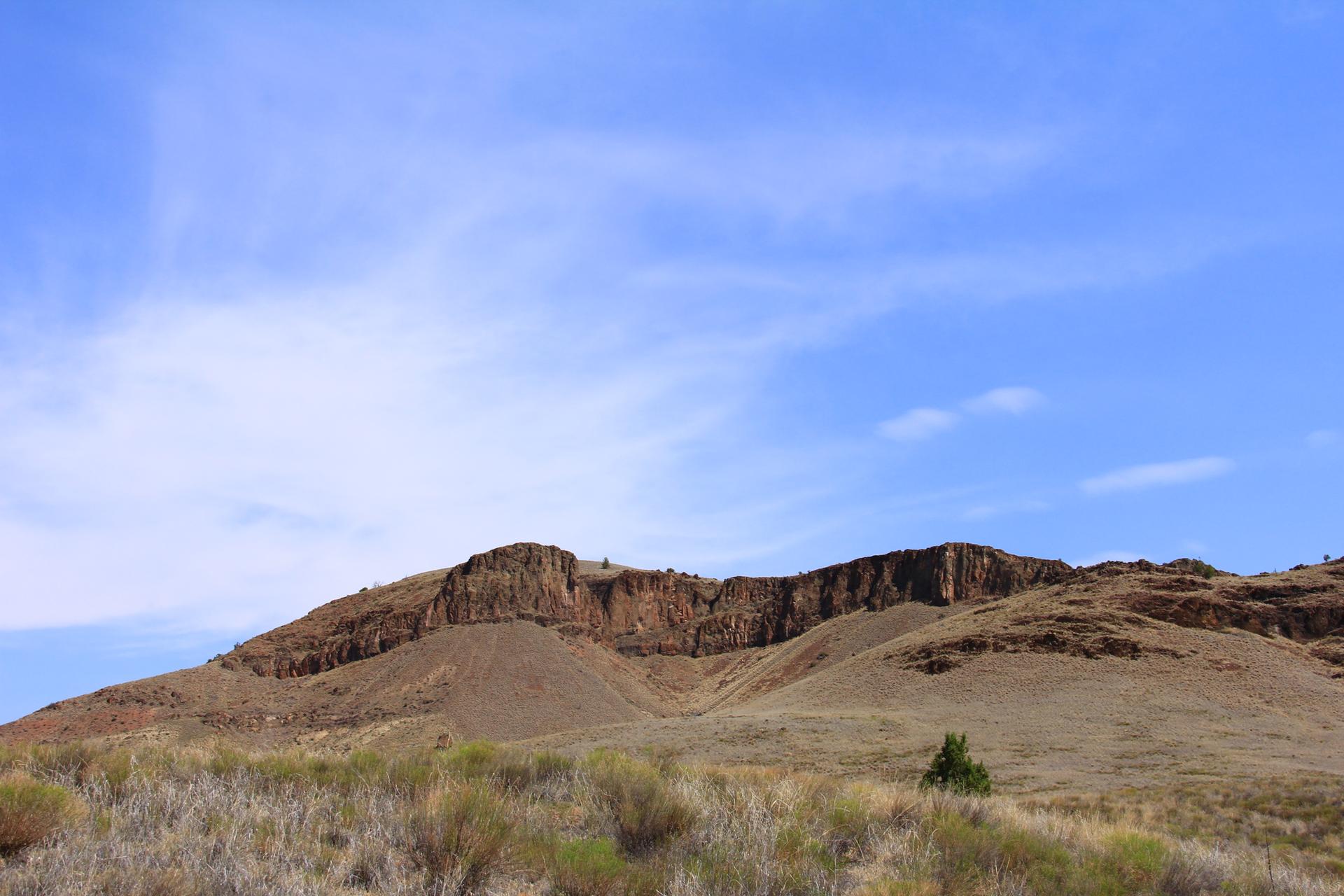 A large rocky cliff face rises under a bright blue sky.