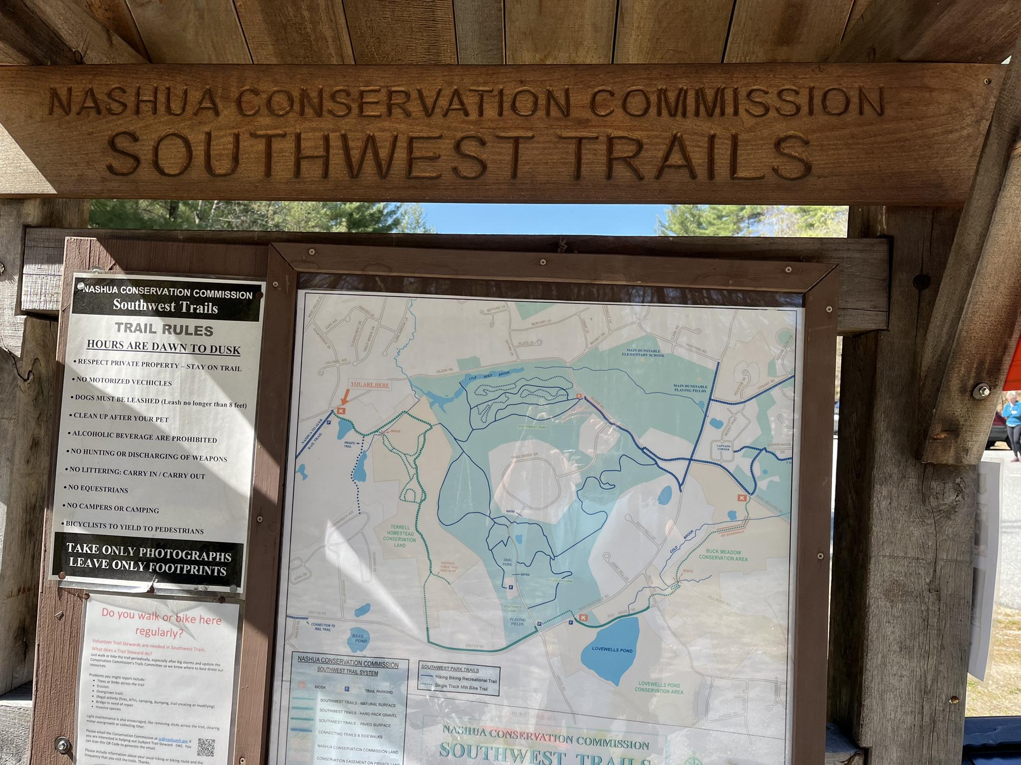 Outdoor wooden sign displaying a trail map and rules on a sunny day.
