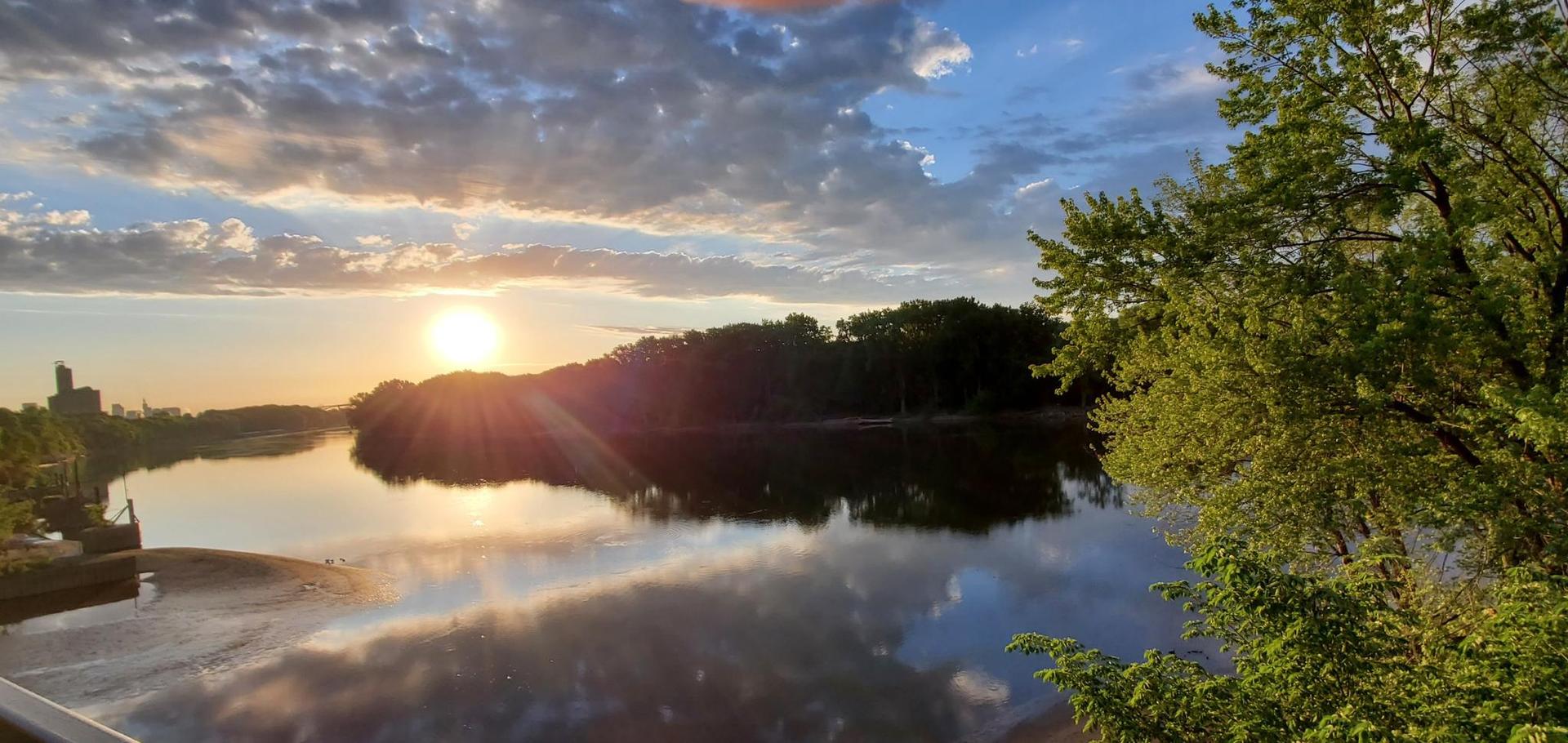 Golden sunset over a calm river, reflecting clouds and trees on the banks.