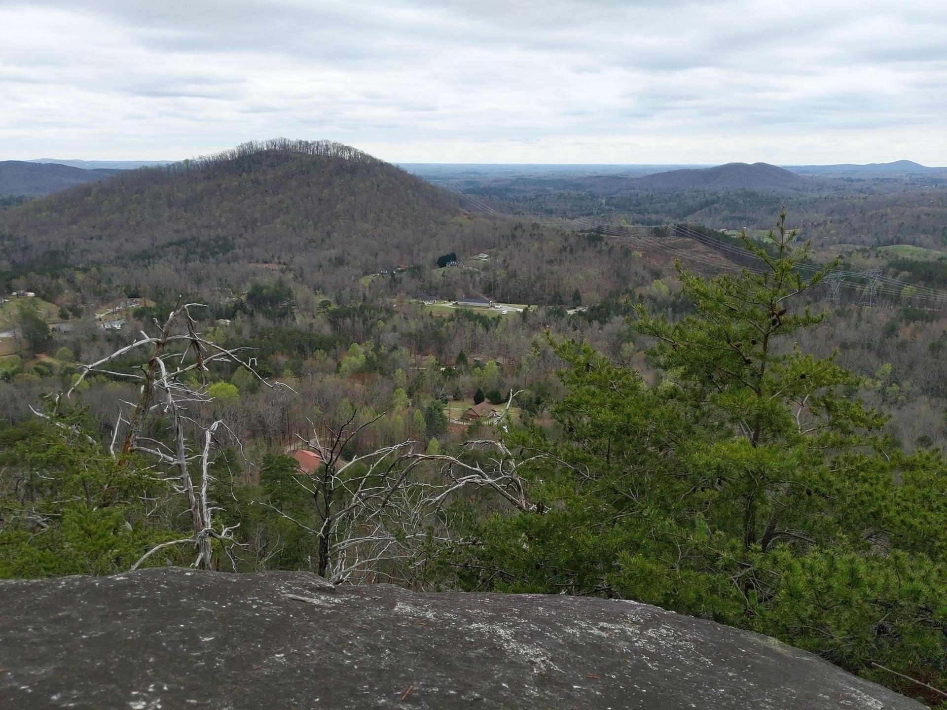Overcast view of forested hills and distant mountains from a rocky outcrop.