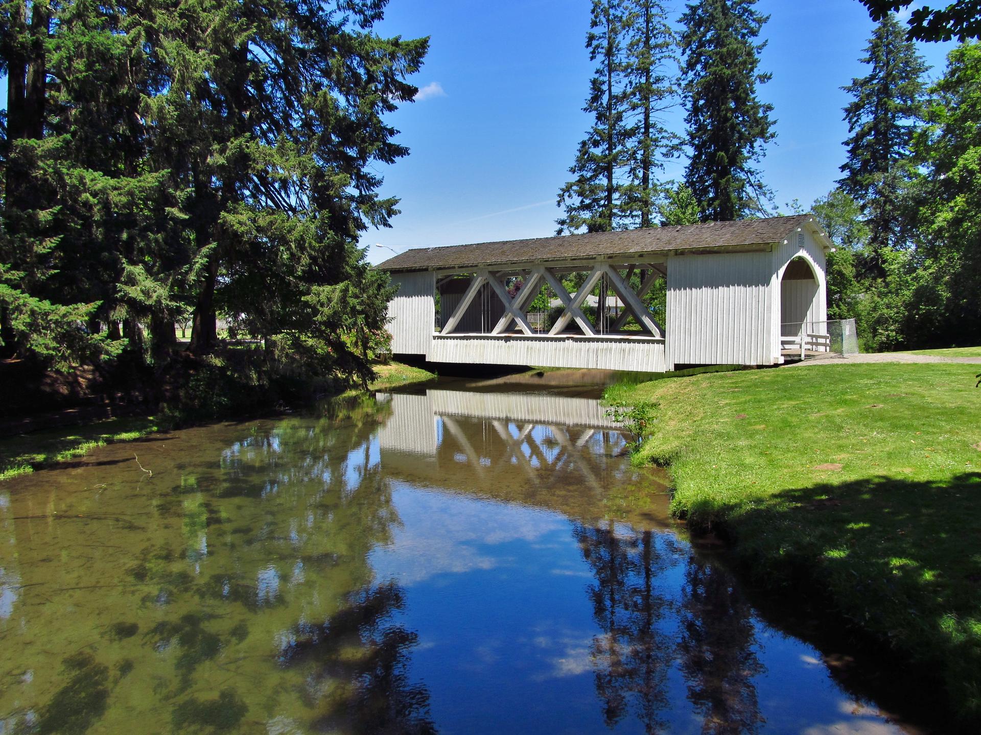 A white covered bridge spans a calm stream on a bright, sunny day.