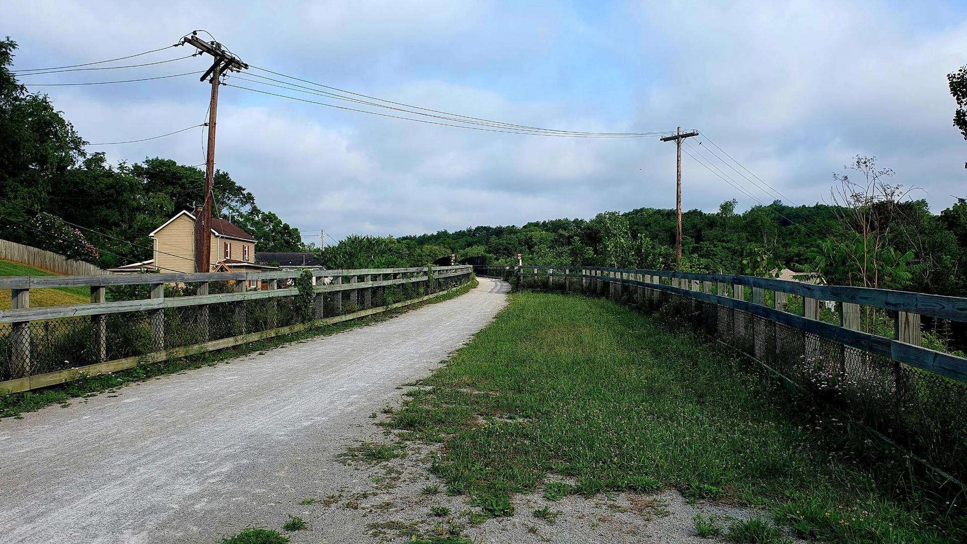 A gravel path with wooden fences, leading past a house under a cloudy sky.