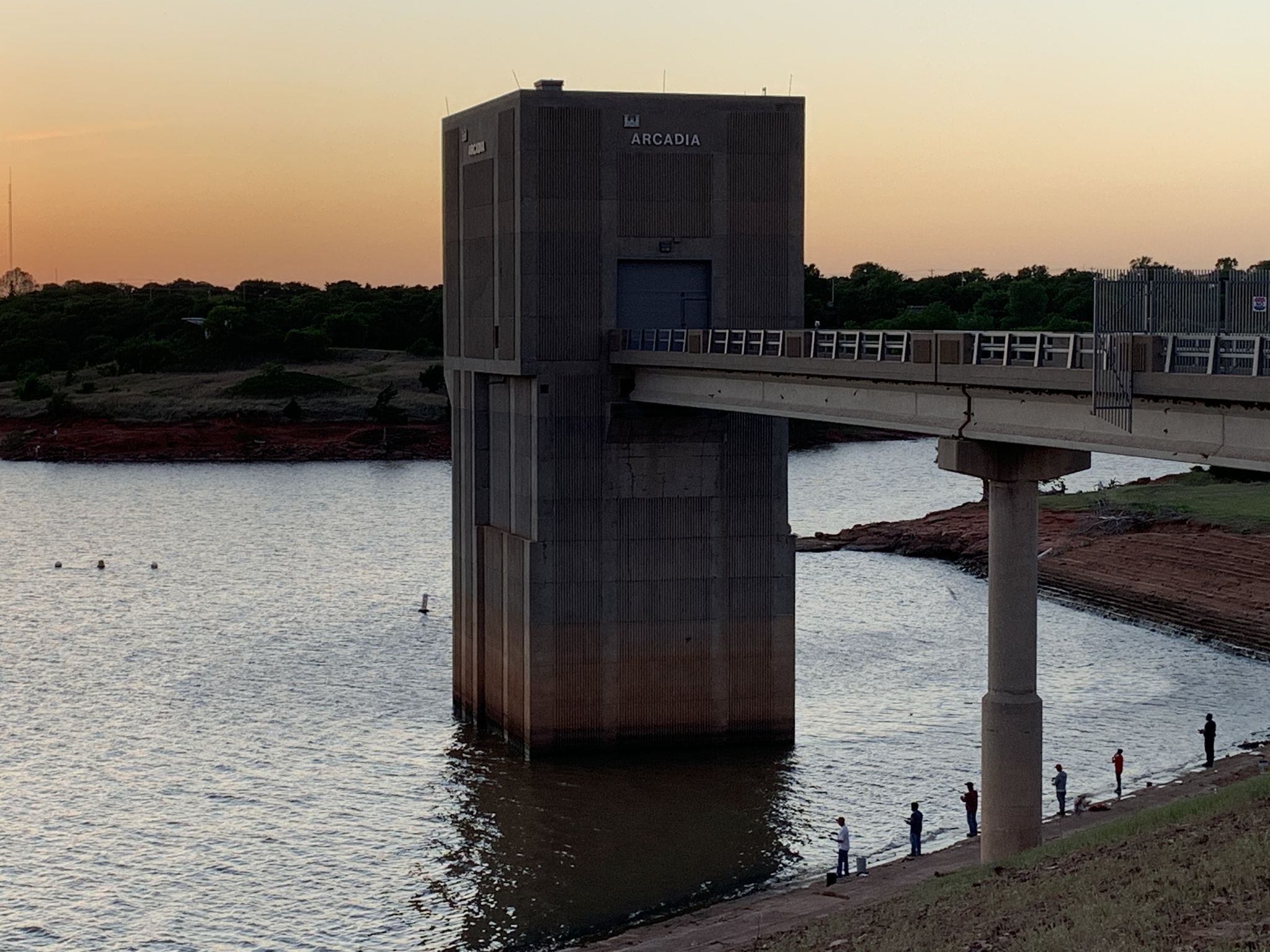 Concrete structure in lake at sunset with people fishing and swimming. - Arcadia Lake Trail
