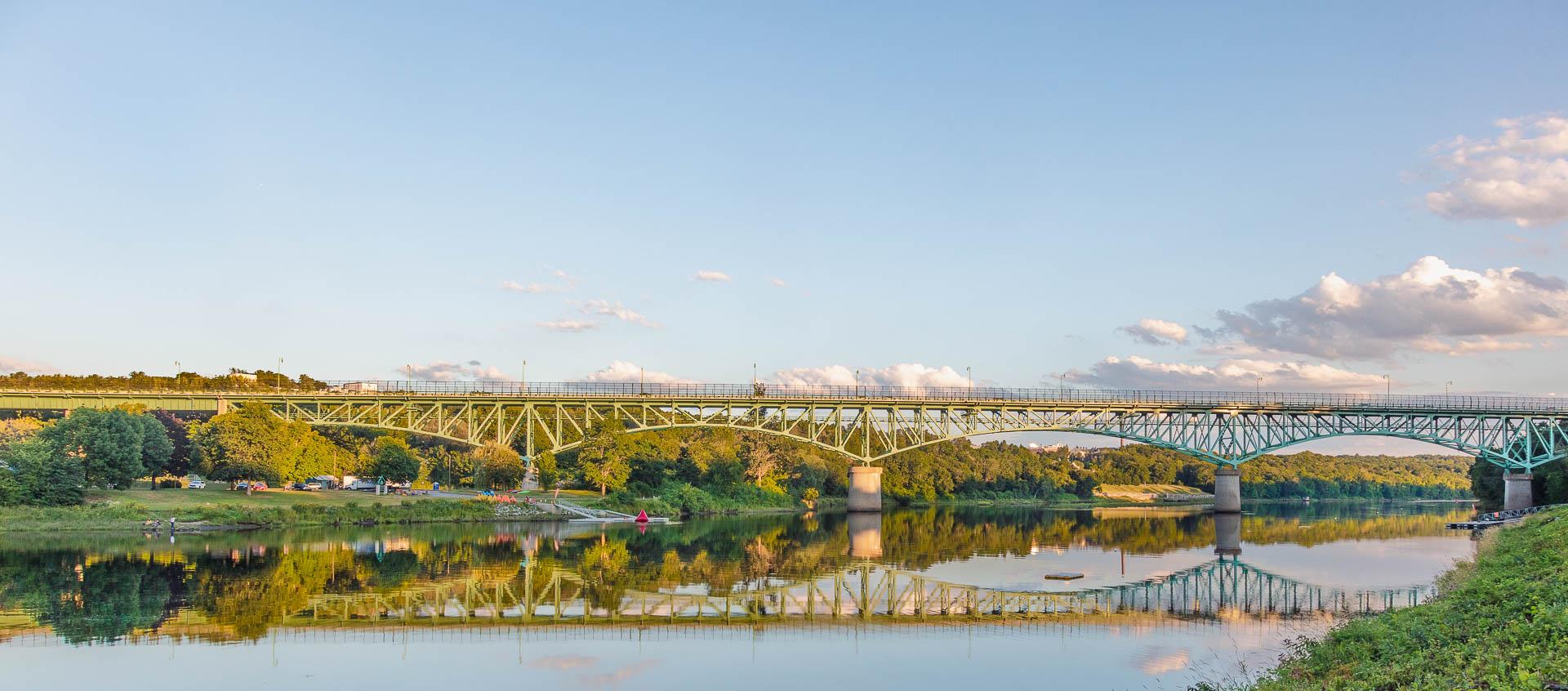 Two large bridges span a wide river under a clear sky at golden hour.