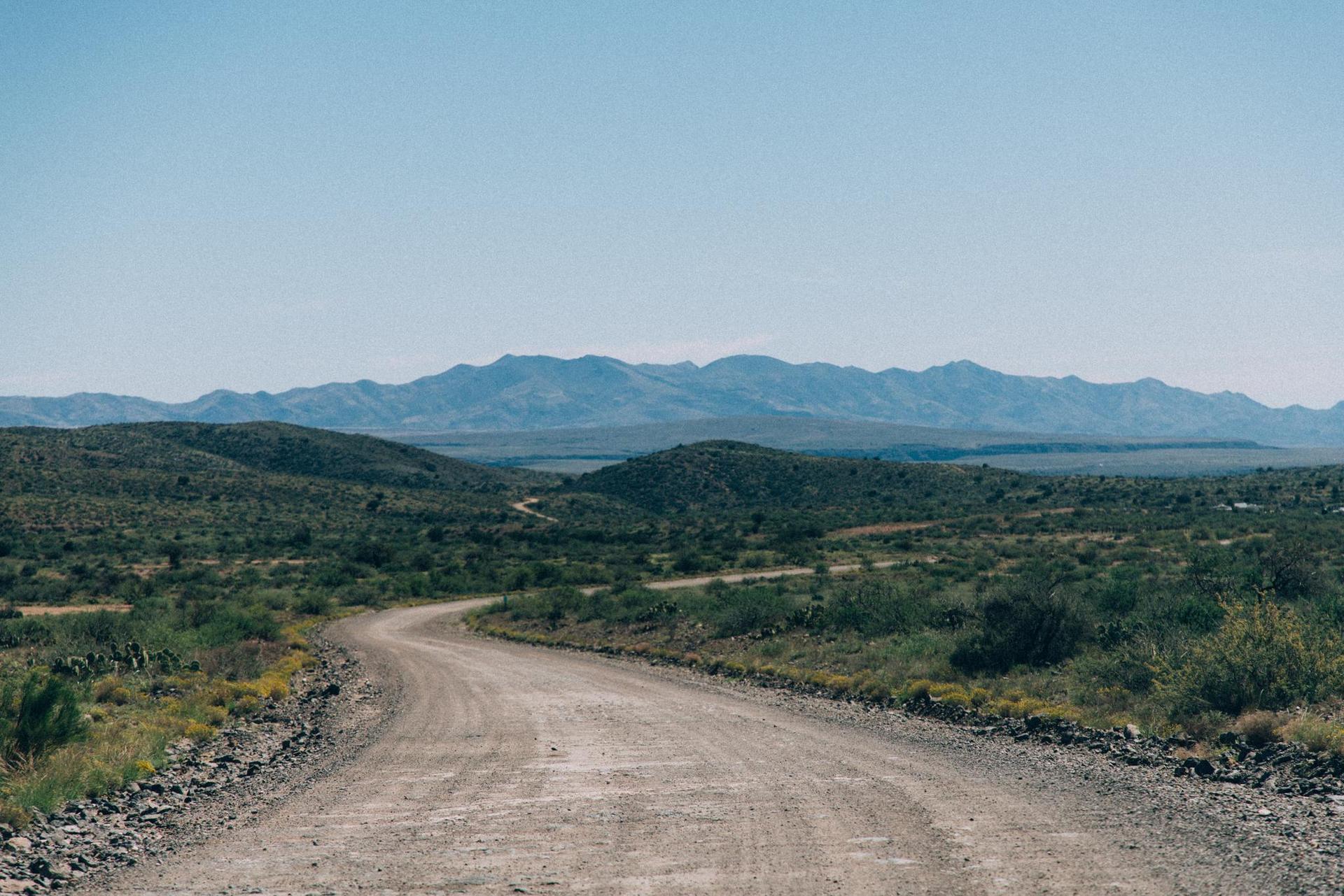 A winding dirt road through arid hills under a clear blue sky.