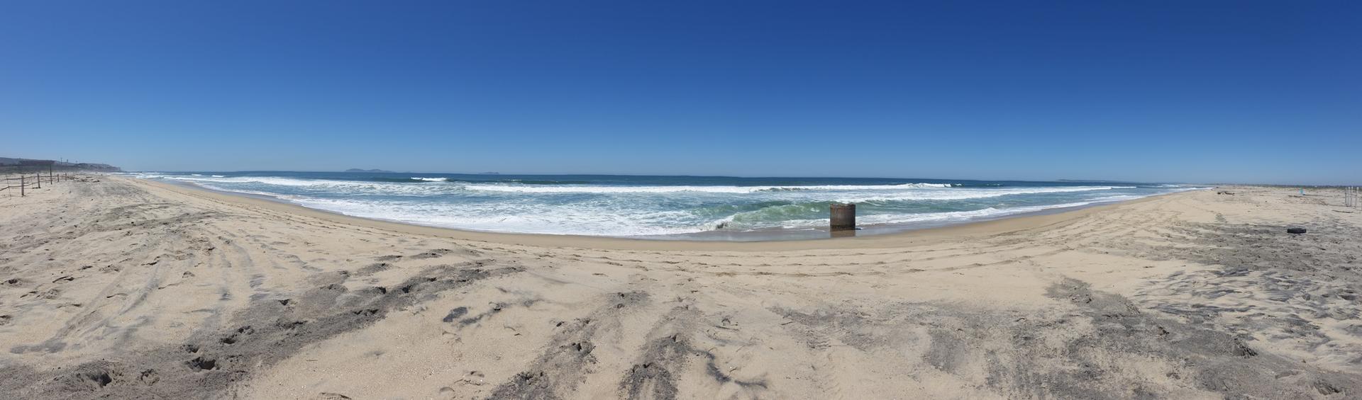 Panoramic view of a wide sandy beach with ocean waves under a clear sky.
