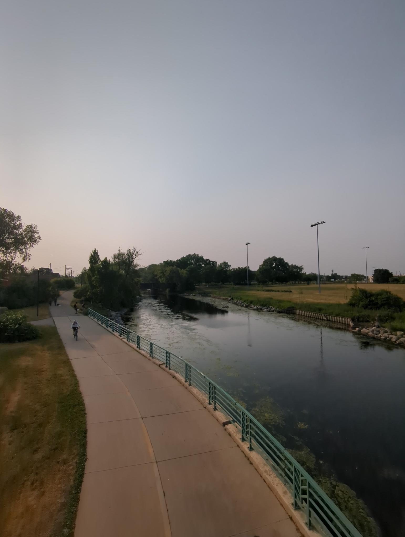 Elevated view of a river, paved path, and a person walking.