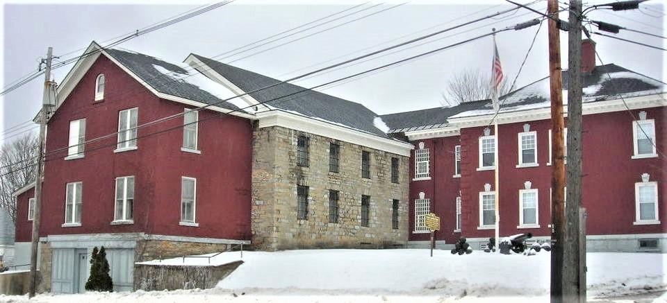 Red and stone building with a flag, surrounded by snow on a cloudy day.