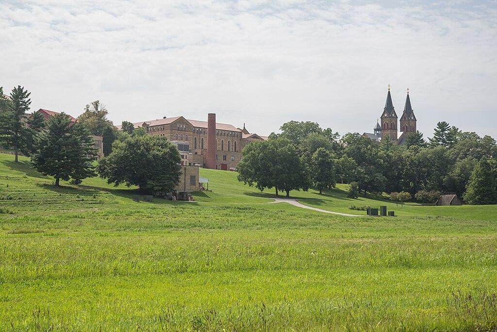 Expansive green grassy hill leading to distant buildings under an overcast sky.