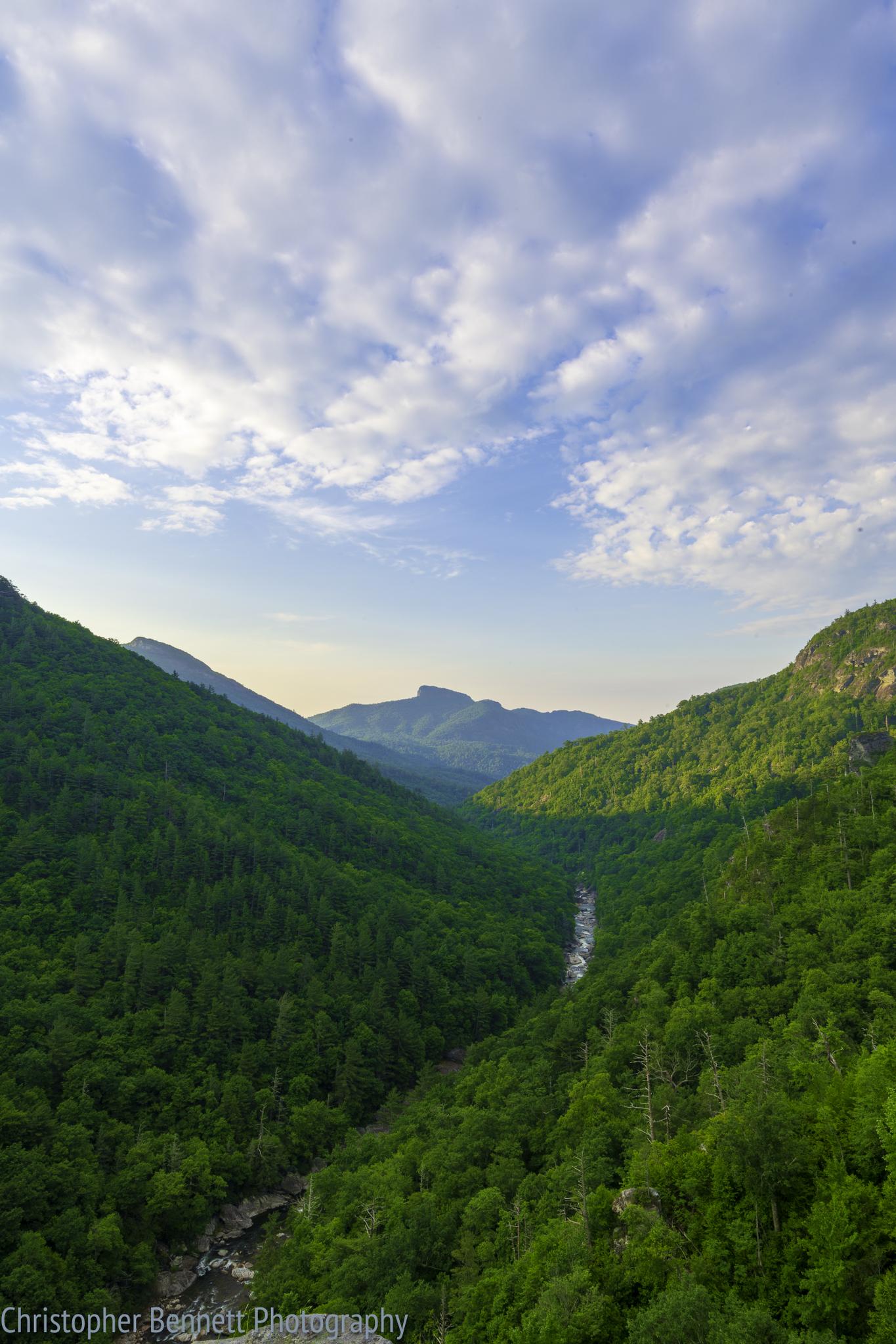 Lush green mountain valley with a winding river under a cloudy sky.