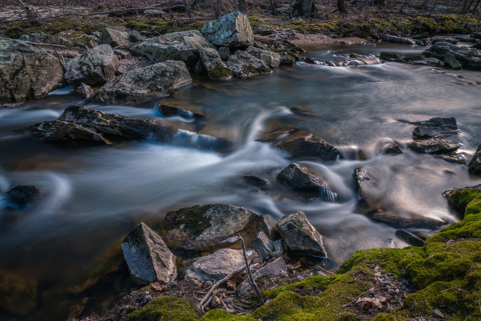 Long exposure of water flowing over mossy rocks in a dark forest.