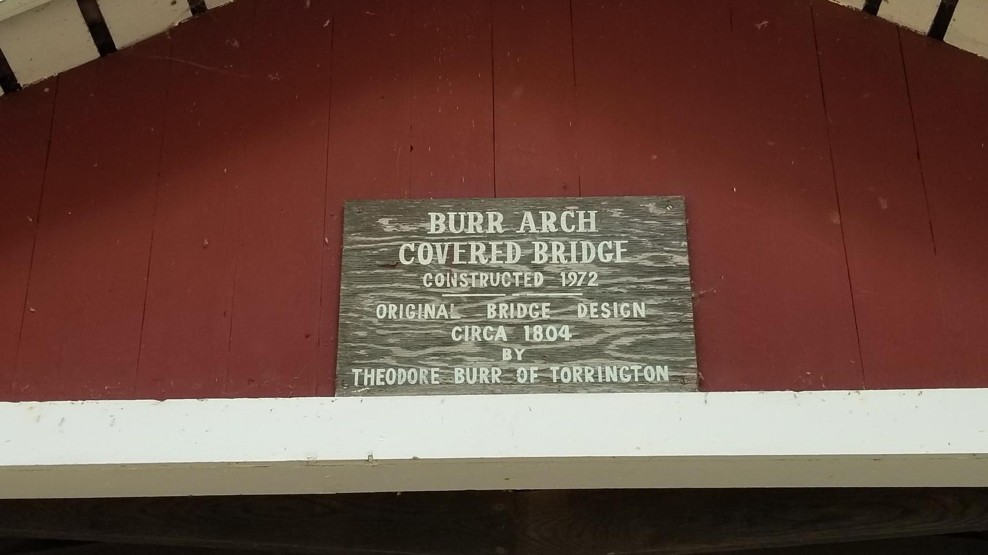 A wooden sign on a red building describes a covered bridge.