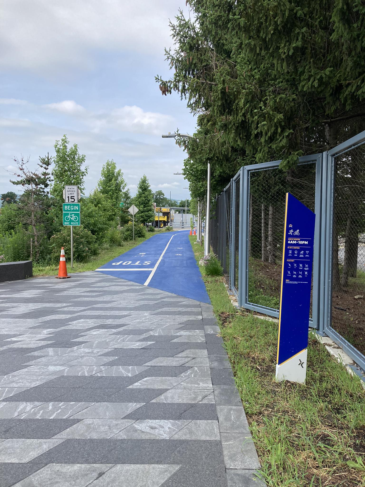Blue paved path with a 'STOP' sign, green trees, and a fence.