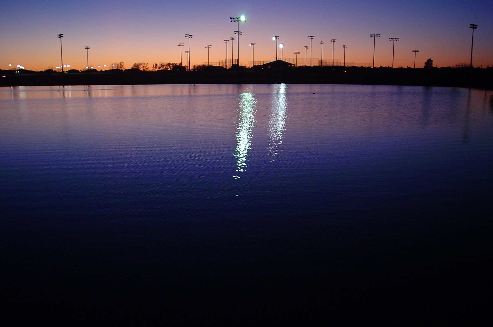 Dusk over a lake reflecting bright stadium lights against an orange-purple sky. - Russell Creek Park Trail