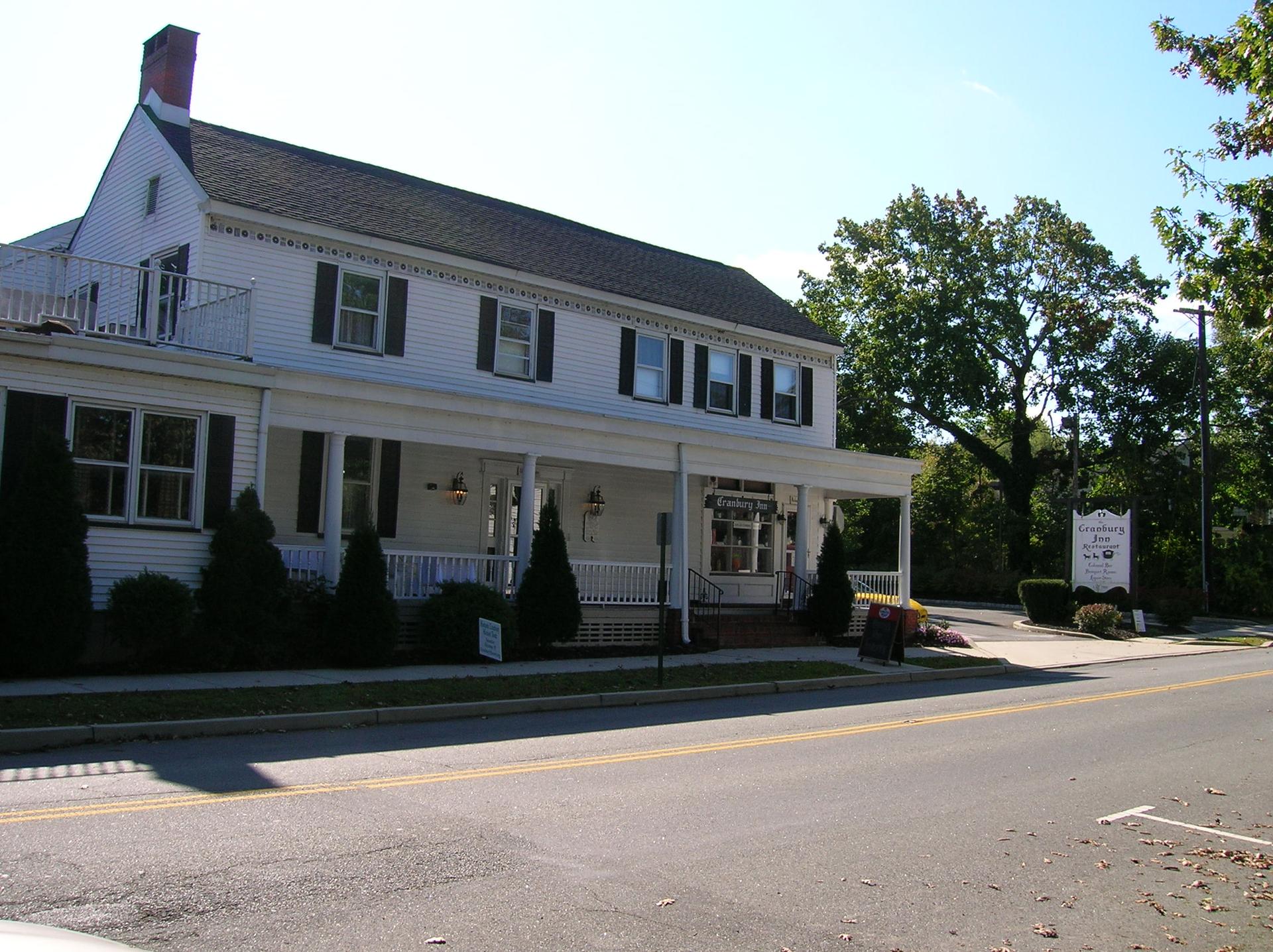 A large white house with a porch next to a road on a sunny day.