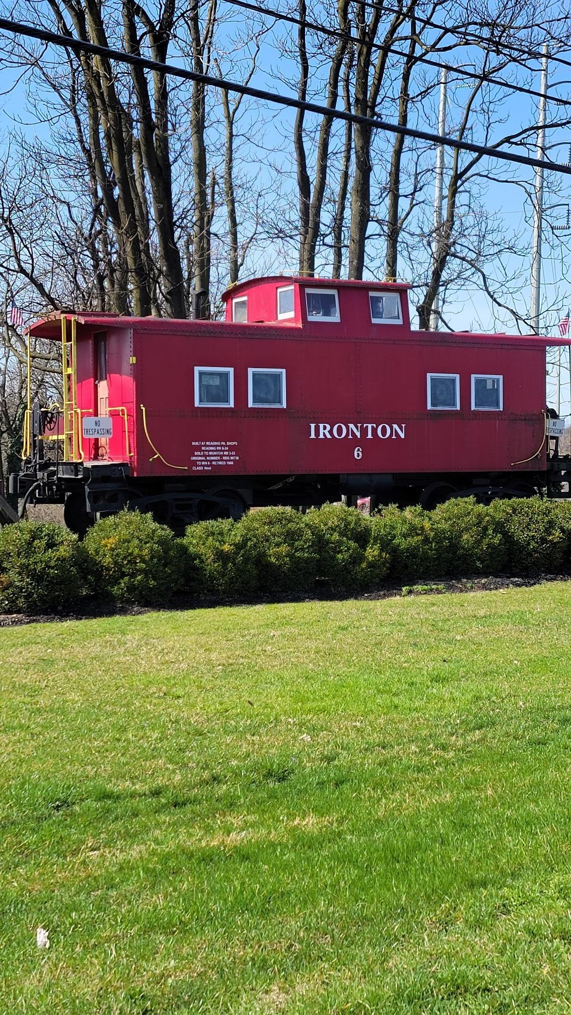 A bright red train caboose sits on green grass under a clear sky.