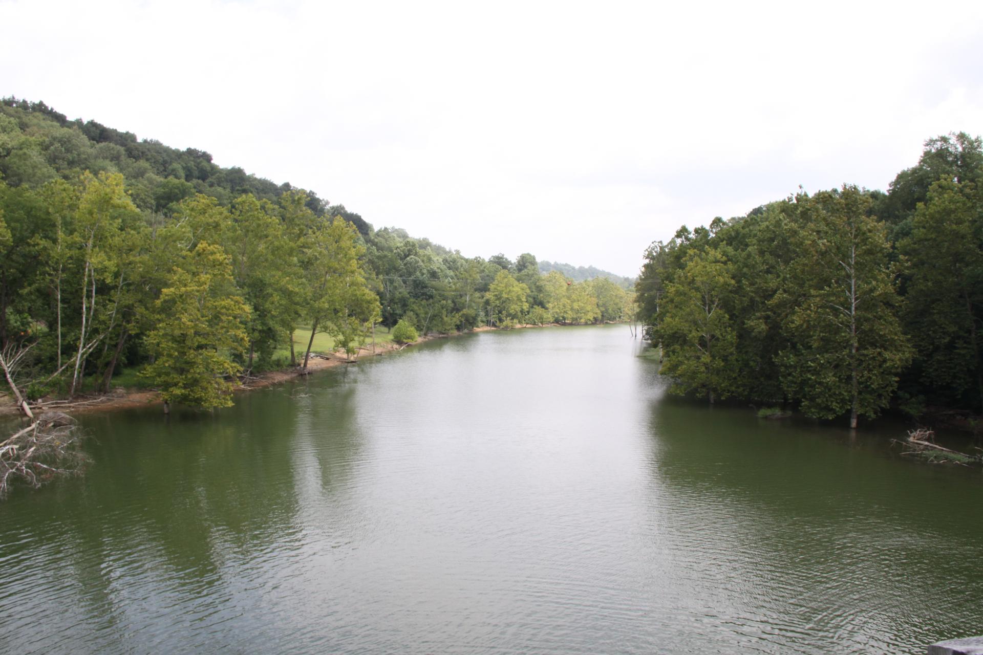 A wide river flows between densely forested hills under an overcast sky.