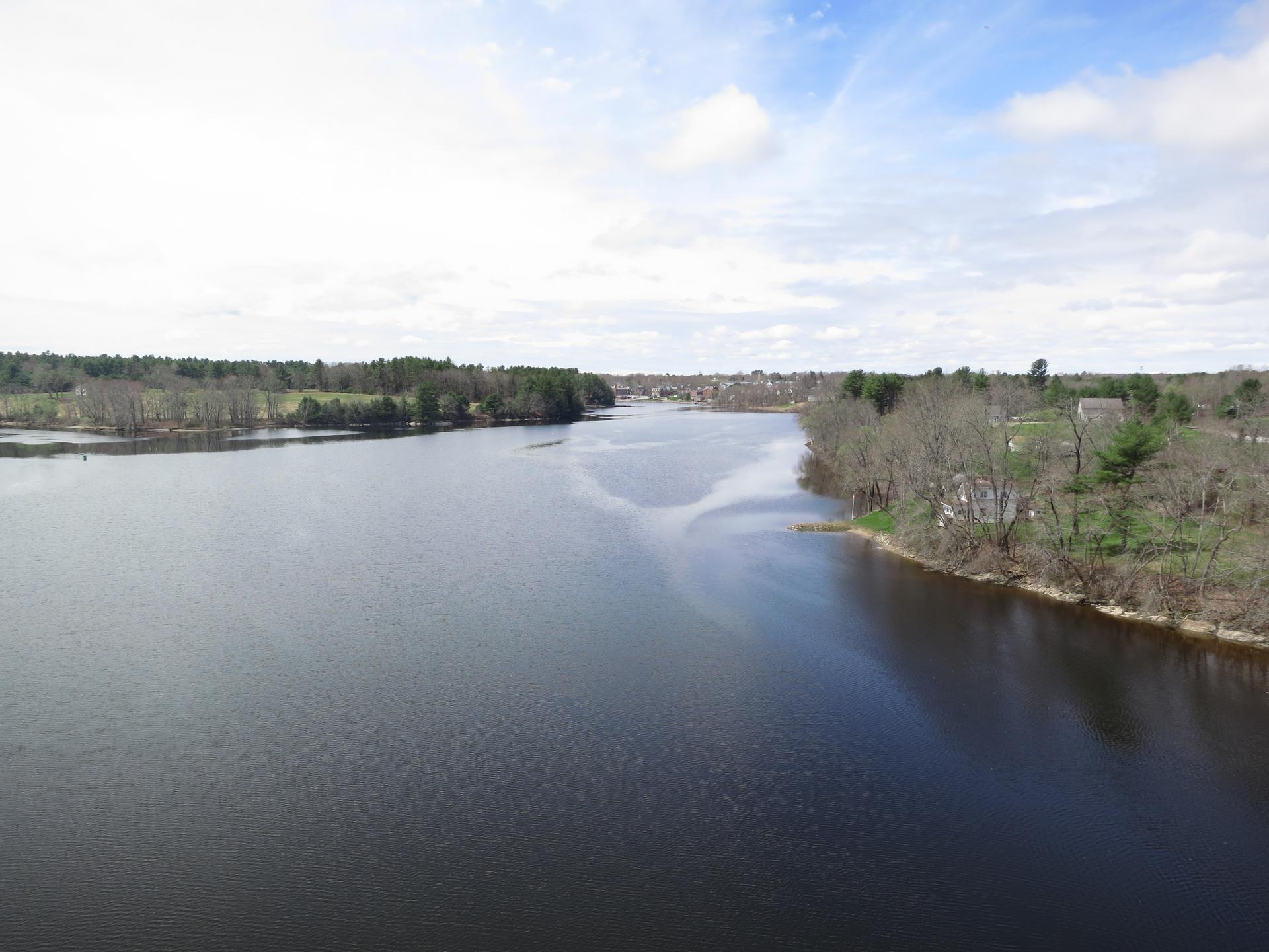 Wide river with tree-lined banks under a partly cloudy sky.
