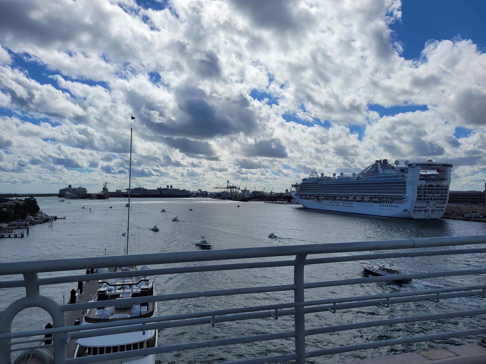 Large cruise ship in a harbor with smaller boats under a cloudy sky.