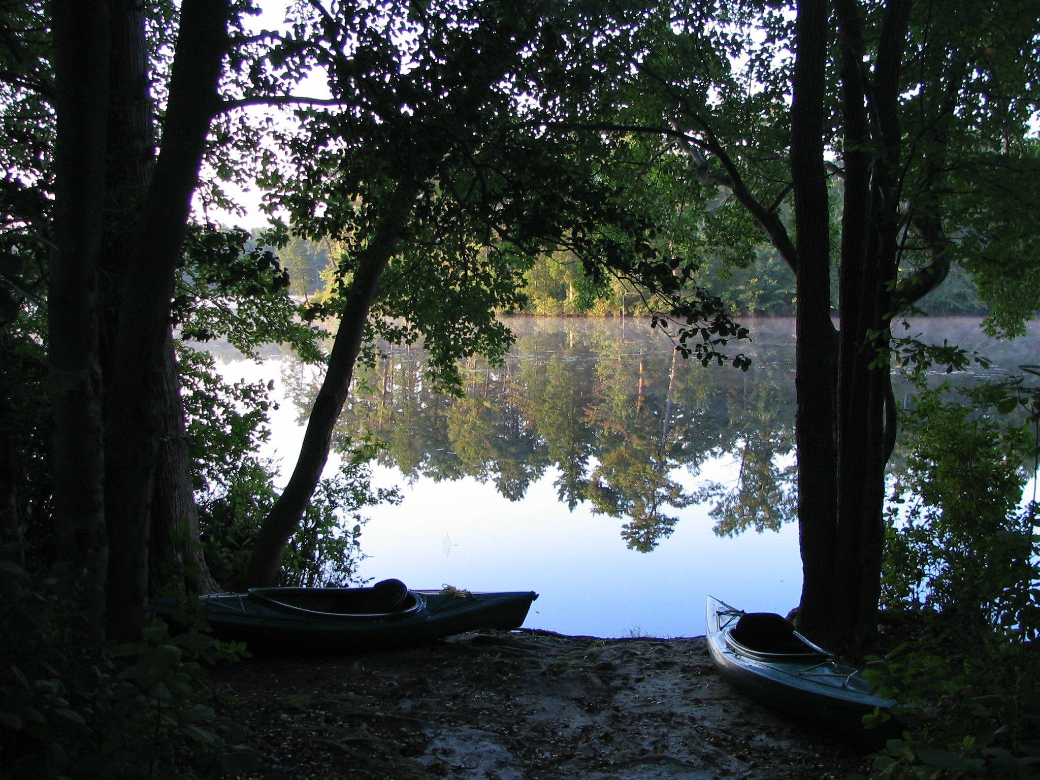 Two kayaks rest on a dark shore beside a calm, reflective lake. - Atsion Lake Blue Trail