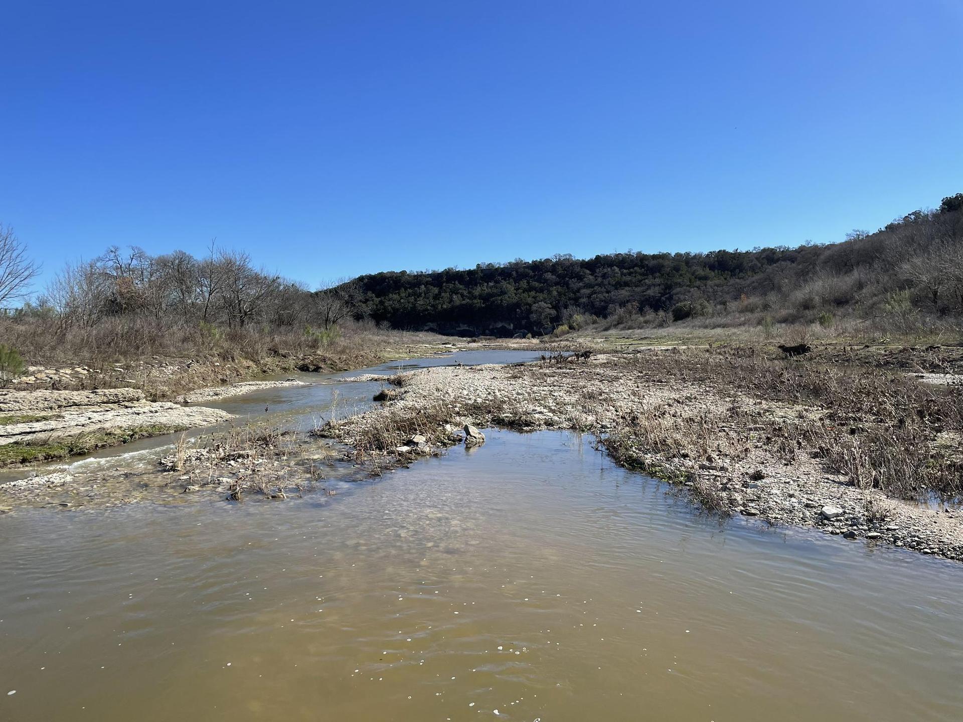 A winding, shallow river in a dry, rocky landscape under a bright blue sky.
