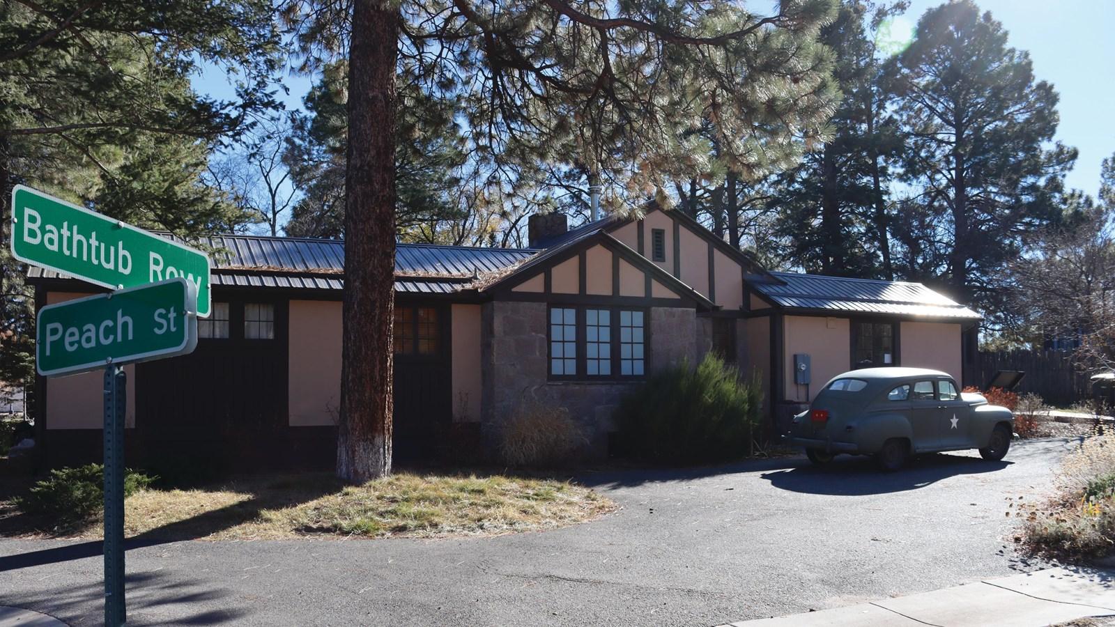 House with a vintage car parked outside, street signs, and pine trees on a sunny day.