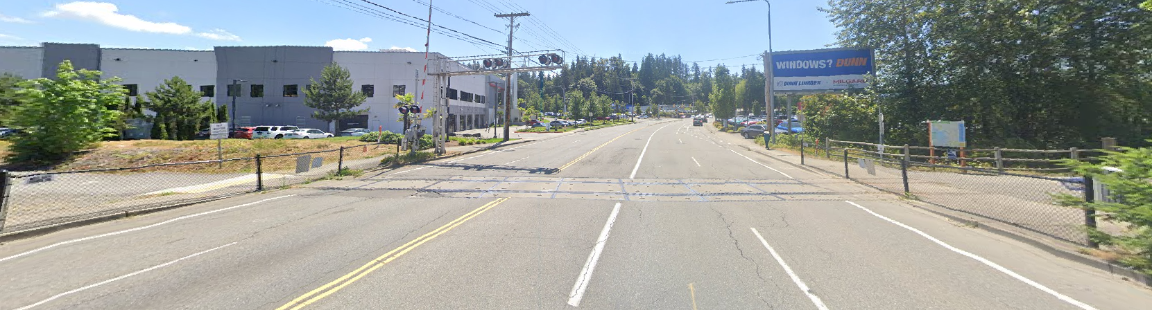 A wide road with industrial buildings and trees under a clear sky.