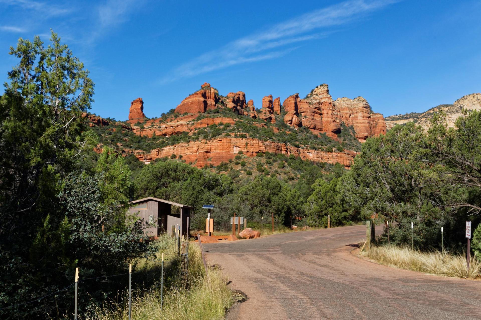 Dirt road leading to red rock formations, with a small building and trees.