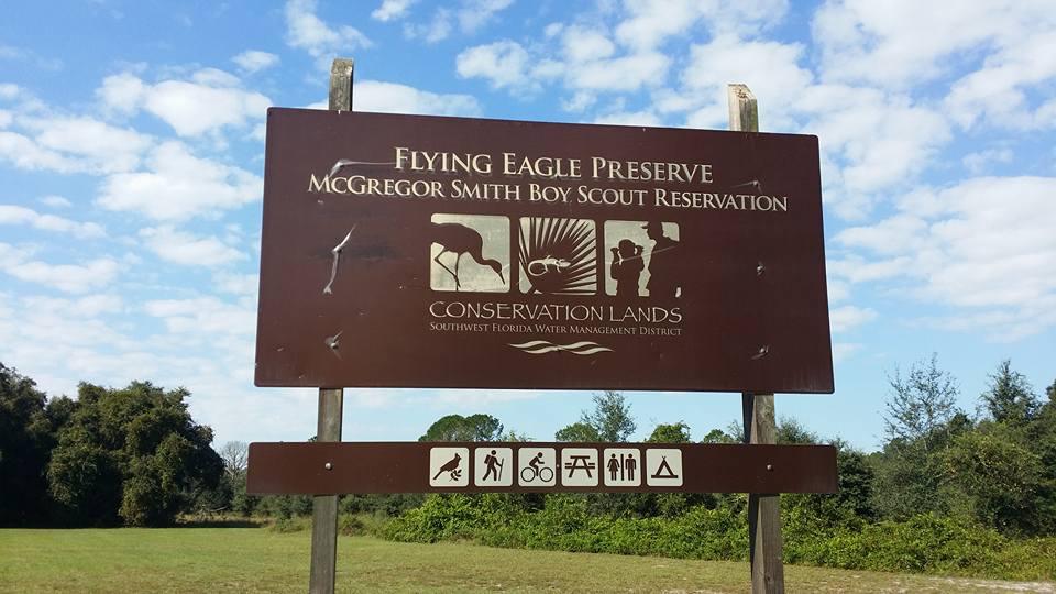 A brown outdoor sign with white text and icons under a bright, cloudy sky.