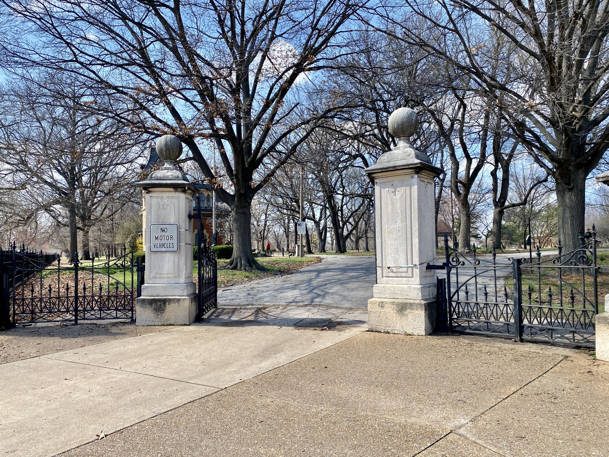 Ornate stone pillars and black gates open to a path under bare trees. - Lafayette Park Loop