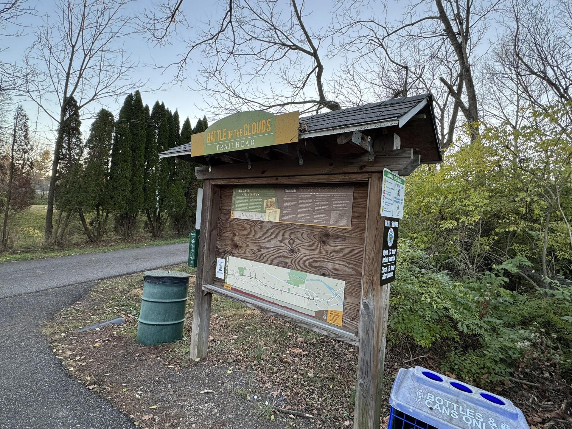A wooden information kiosk stands beside a path with bare trees.