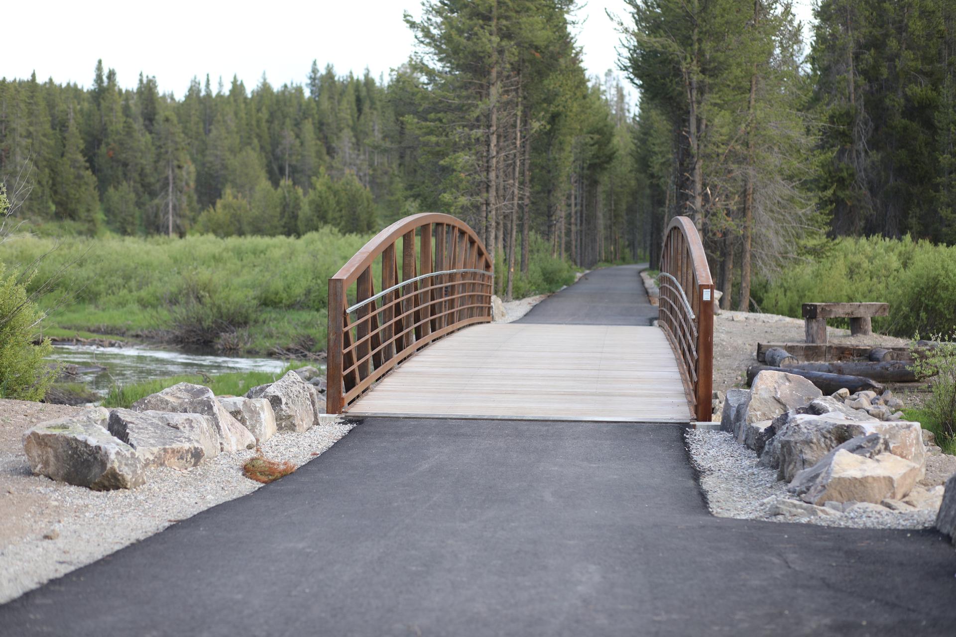 Arched pedestrian bridge over a river, surrounded by forest and rocks.