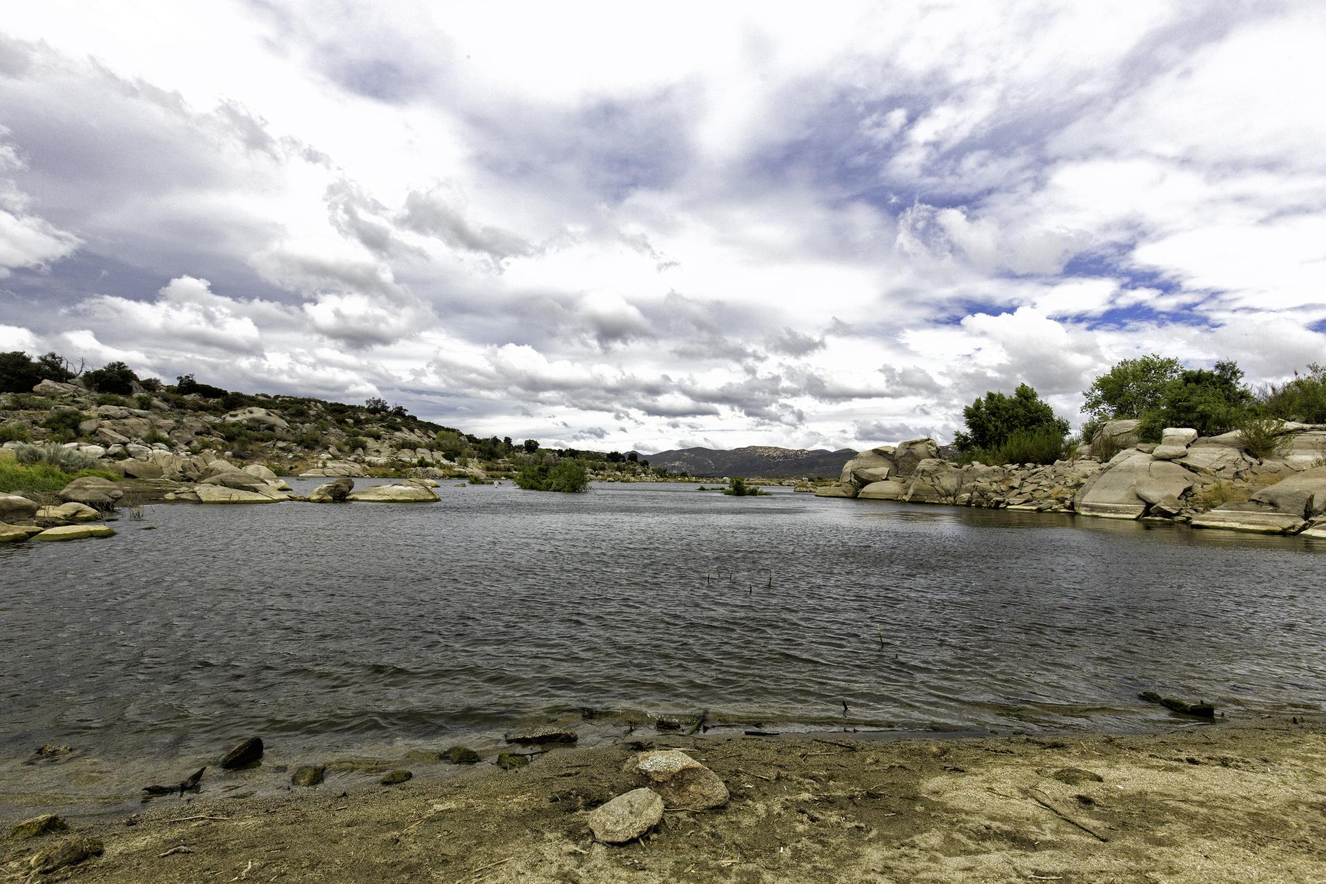 A wide body of water with rocky shores under a dramatic, cloudy sky.