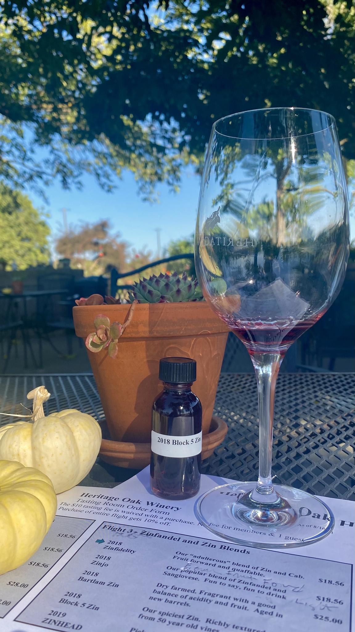 A wine glass, small bottle, and decorative pumpkins on an outdoor table.
