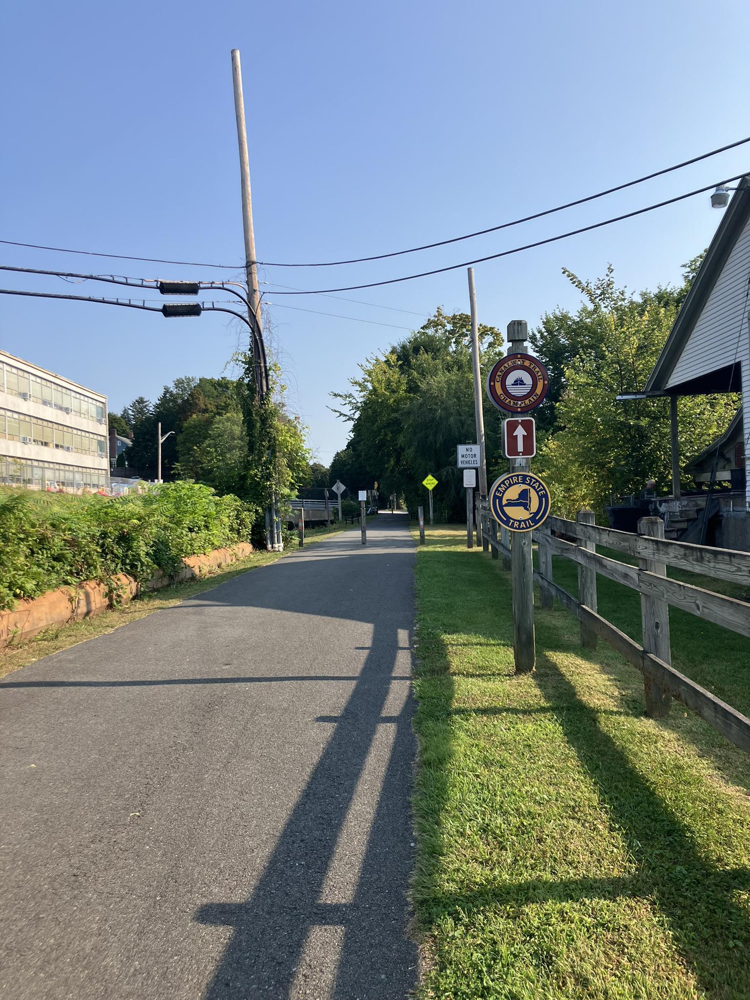 Paved path with trail signs and power lines on a bright, sunny day.