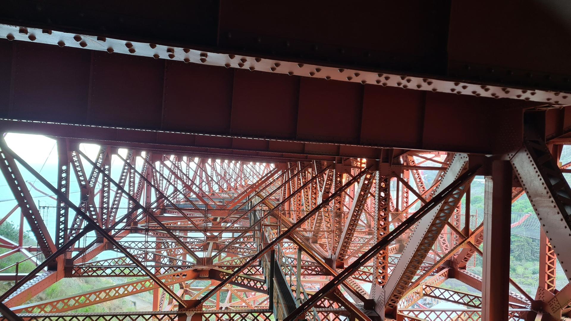 Intricate red metal structure of a large bridge under bright light.