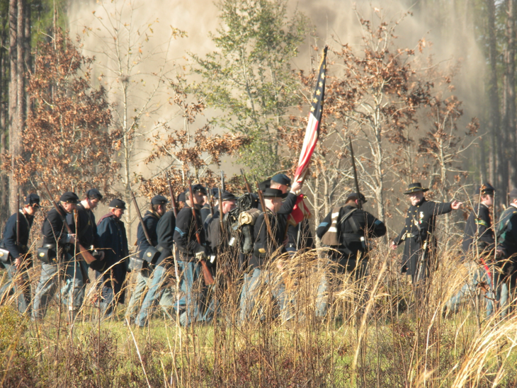 Men in historical military uniforms march through a smoky, wooded landscape.