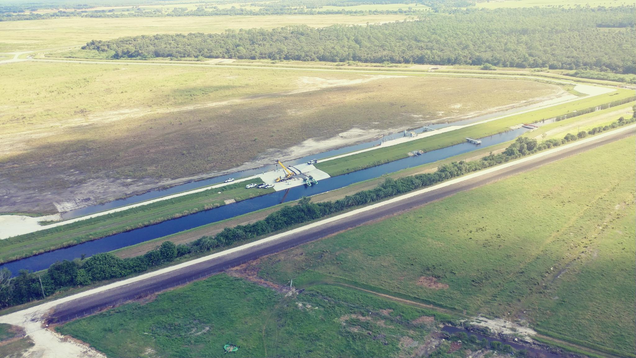 Aerial view of a long canal through green fields and a road.
