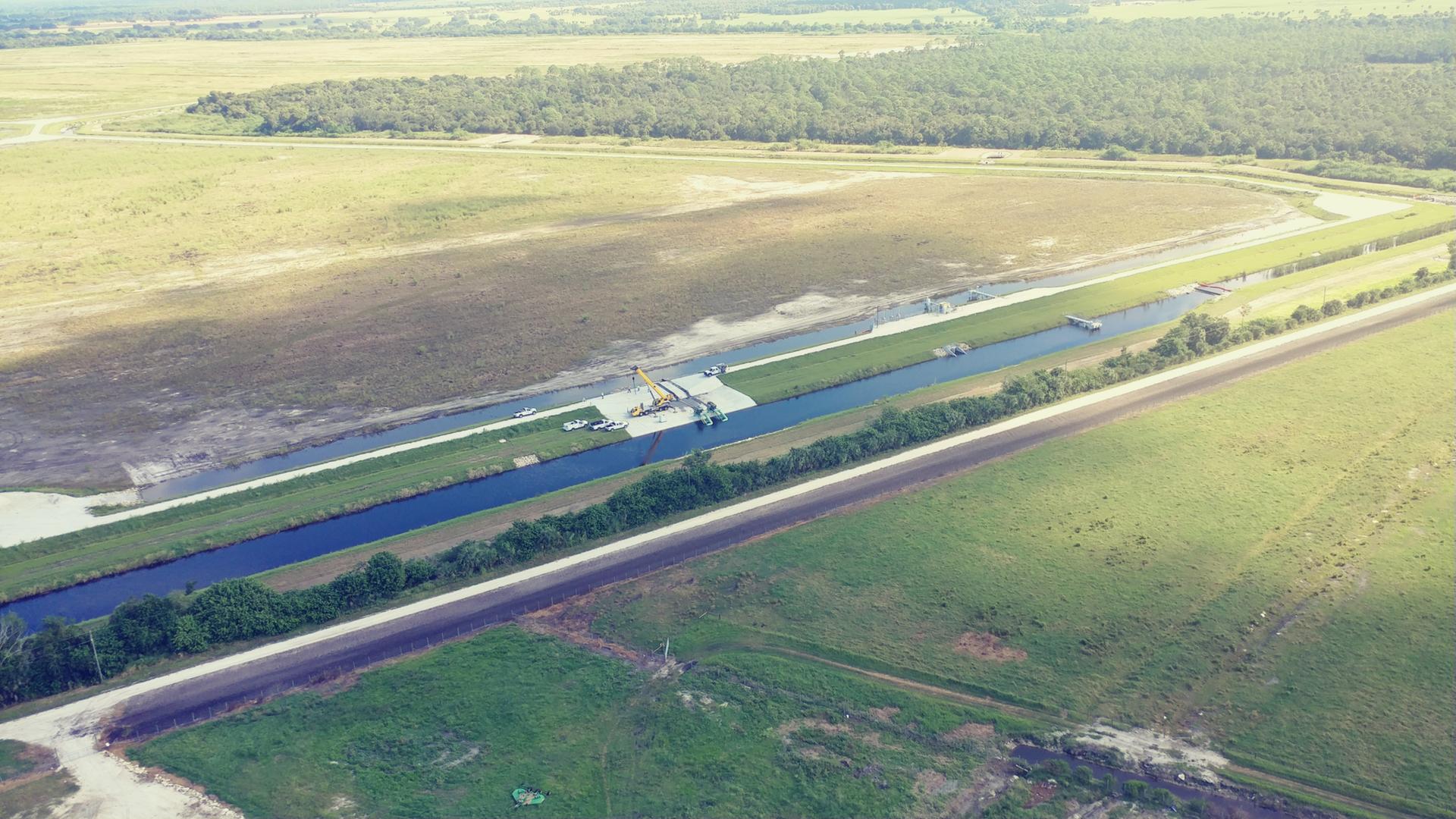Aerial view of a long canal through green fields and a road.