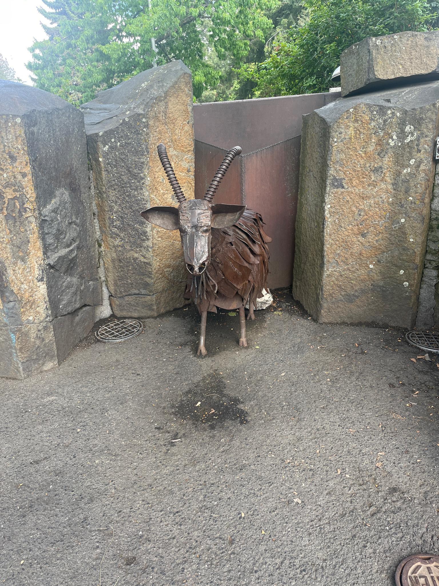 Metal sculpture of a horned animal standing between large stone blocks.