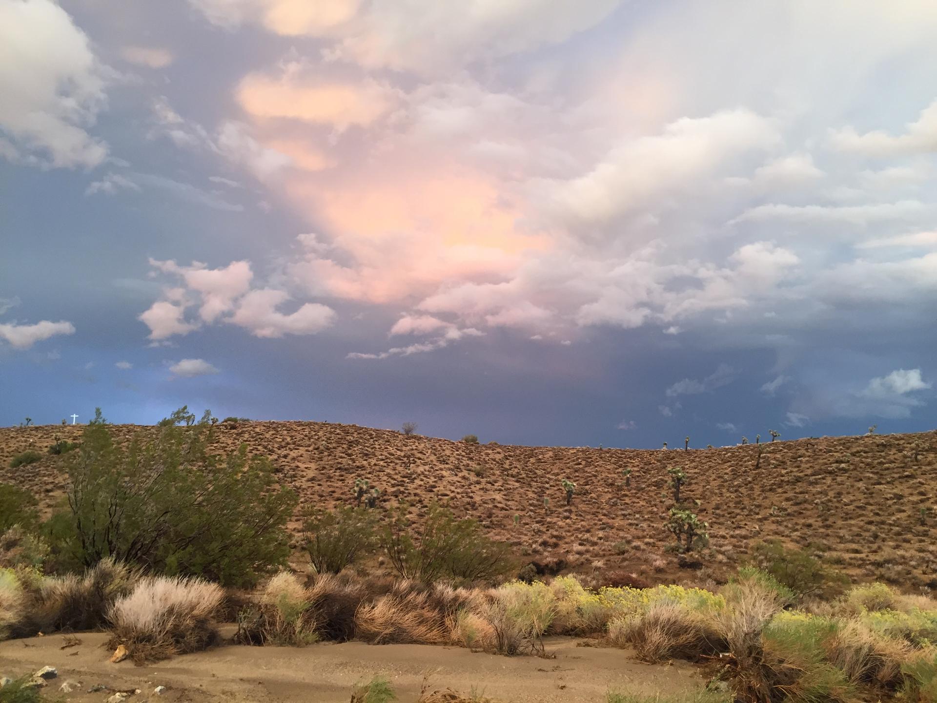 Desert hills under a dramatic sky with storm clouds and pink light.