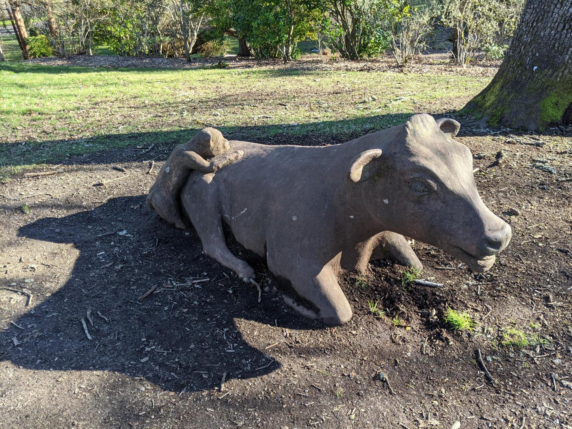 Brightly lit stone sculpture of a cow and small figure on grassy ground.