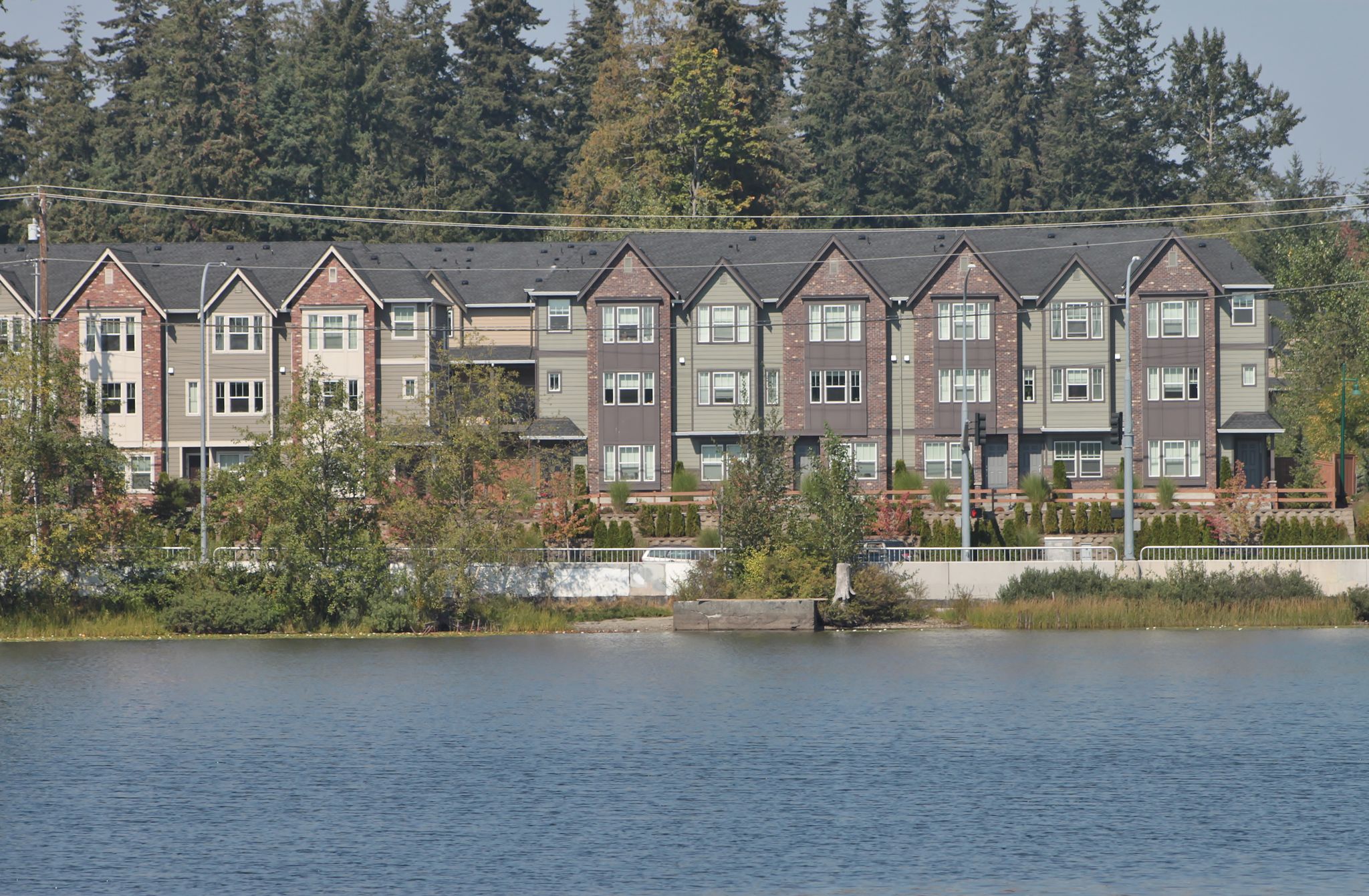A row of modern townhouses overlooks a wide body of water and evergreen trees. - Silver Lake - Mill Creek loop