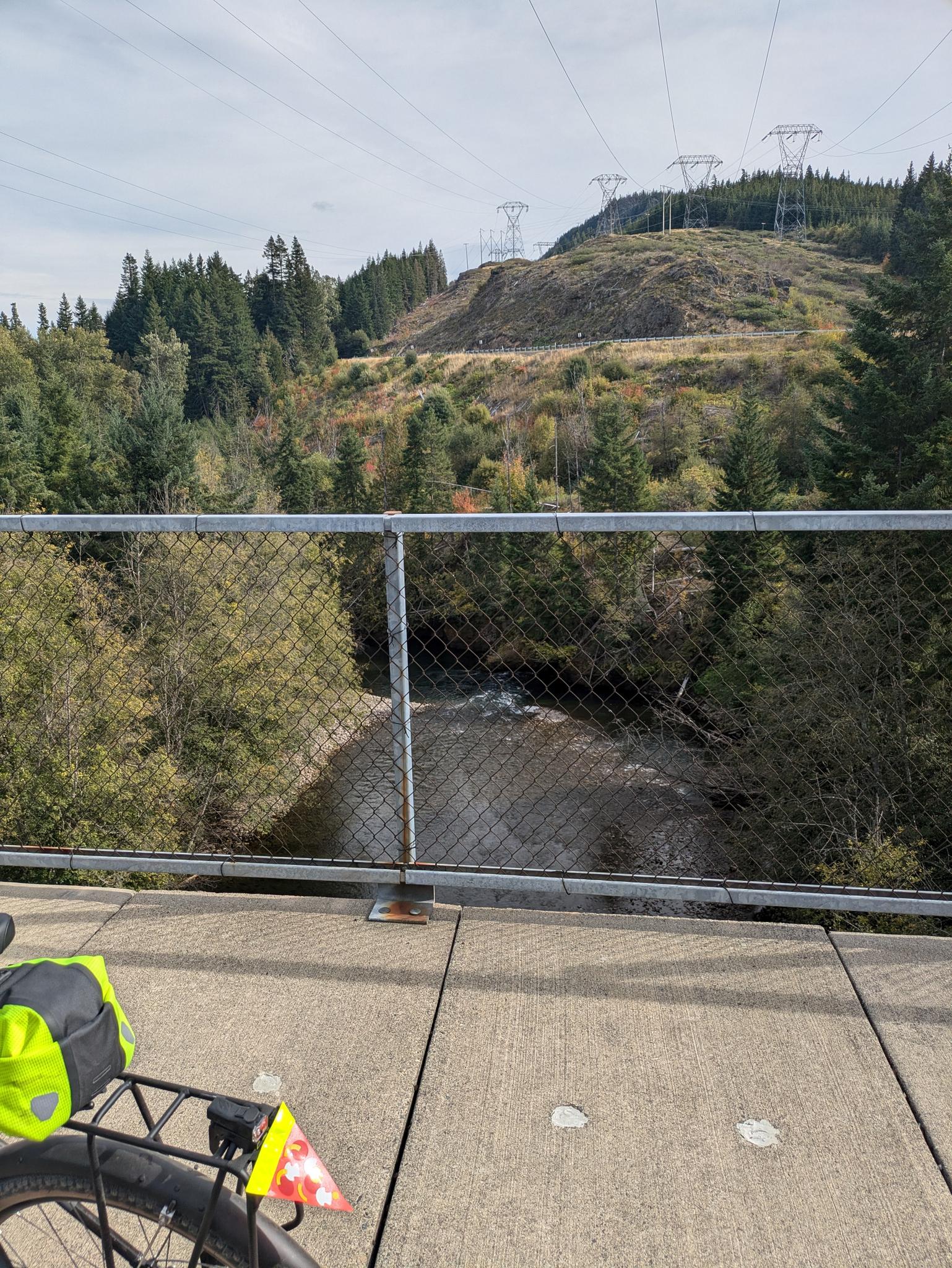 View from a bridge showing a river, forested hills, and power lines.