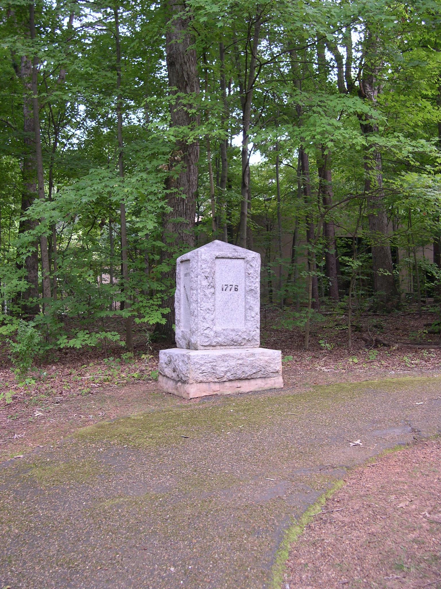 Stone monument with "1772" carved, surrounded by dense green forest, dappled light.