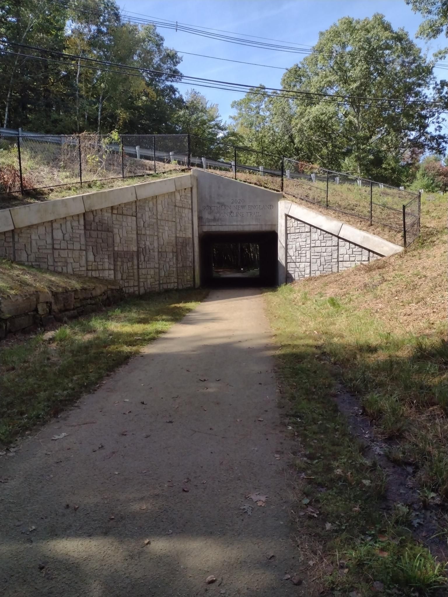 Sunny view of a concrete underpass with a dirt path. - Southern New England Trunkline Trail