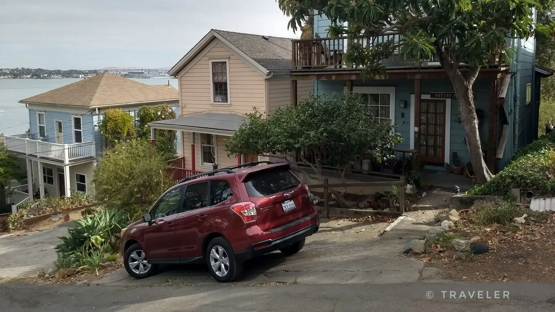 Red SUV parked on a residential street with houses and water in background.