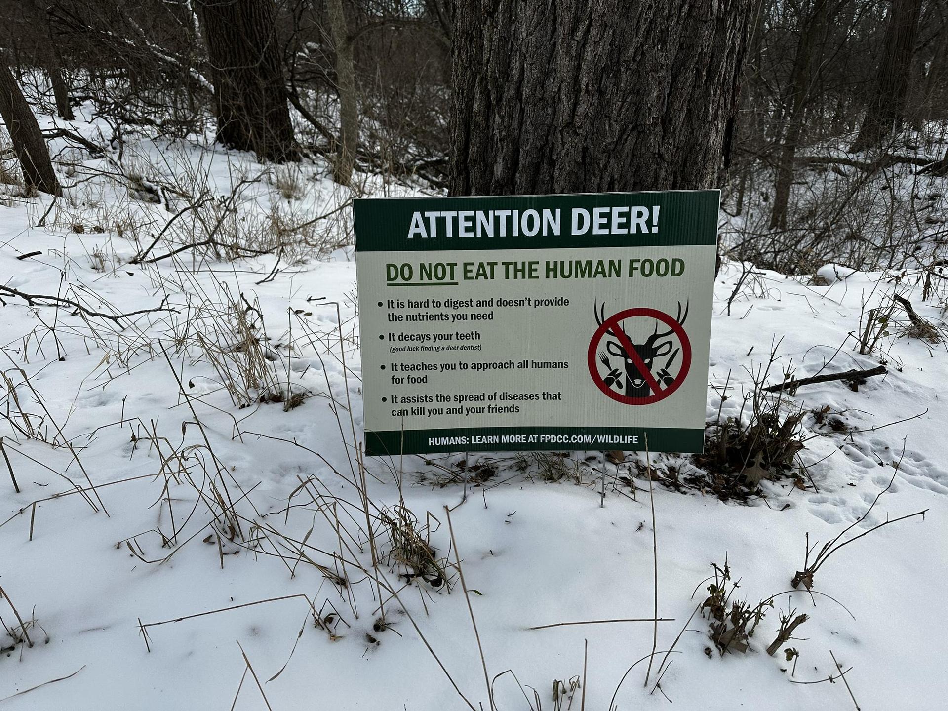 A sign warning "Attention Deer! Do Not Eat The Human Food" in snow.