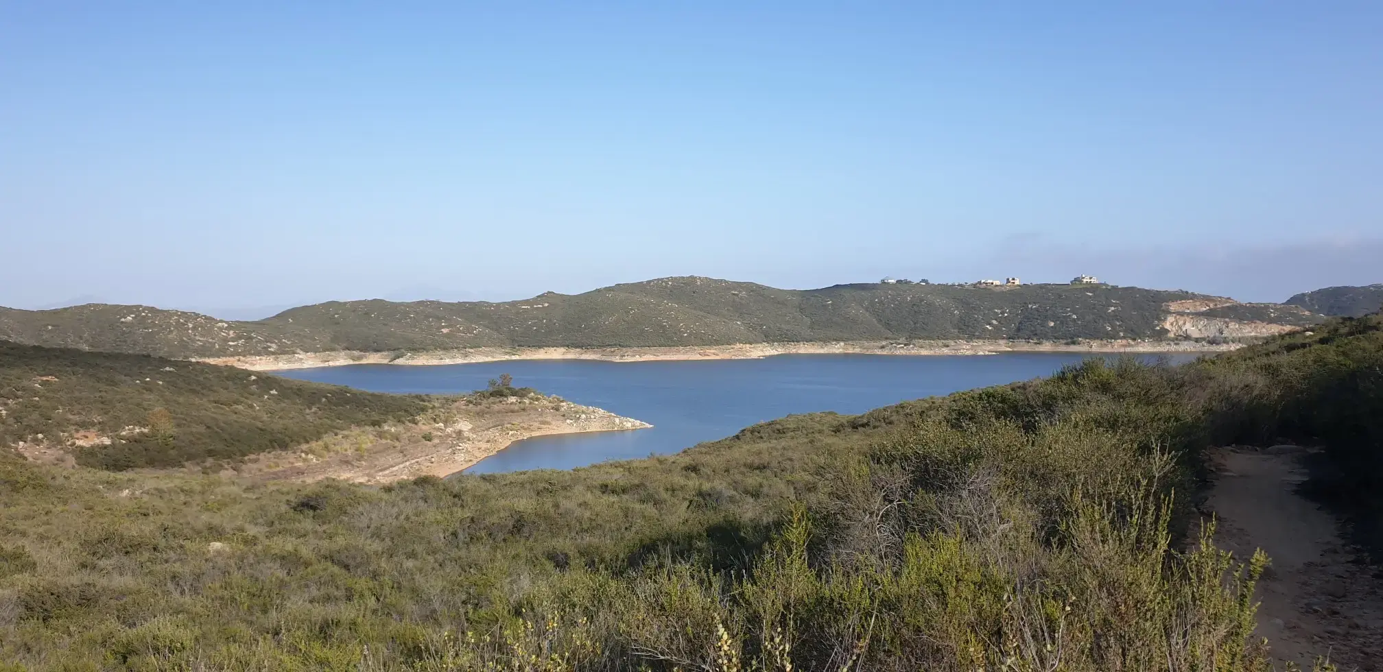 Panoramic view of a calm blue lake surrounded by green and brown hills.